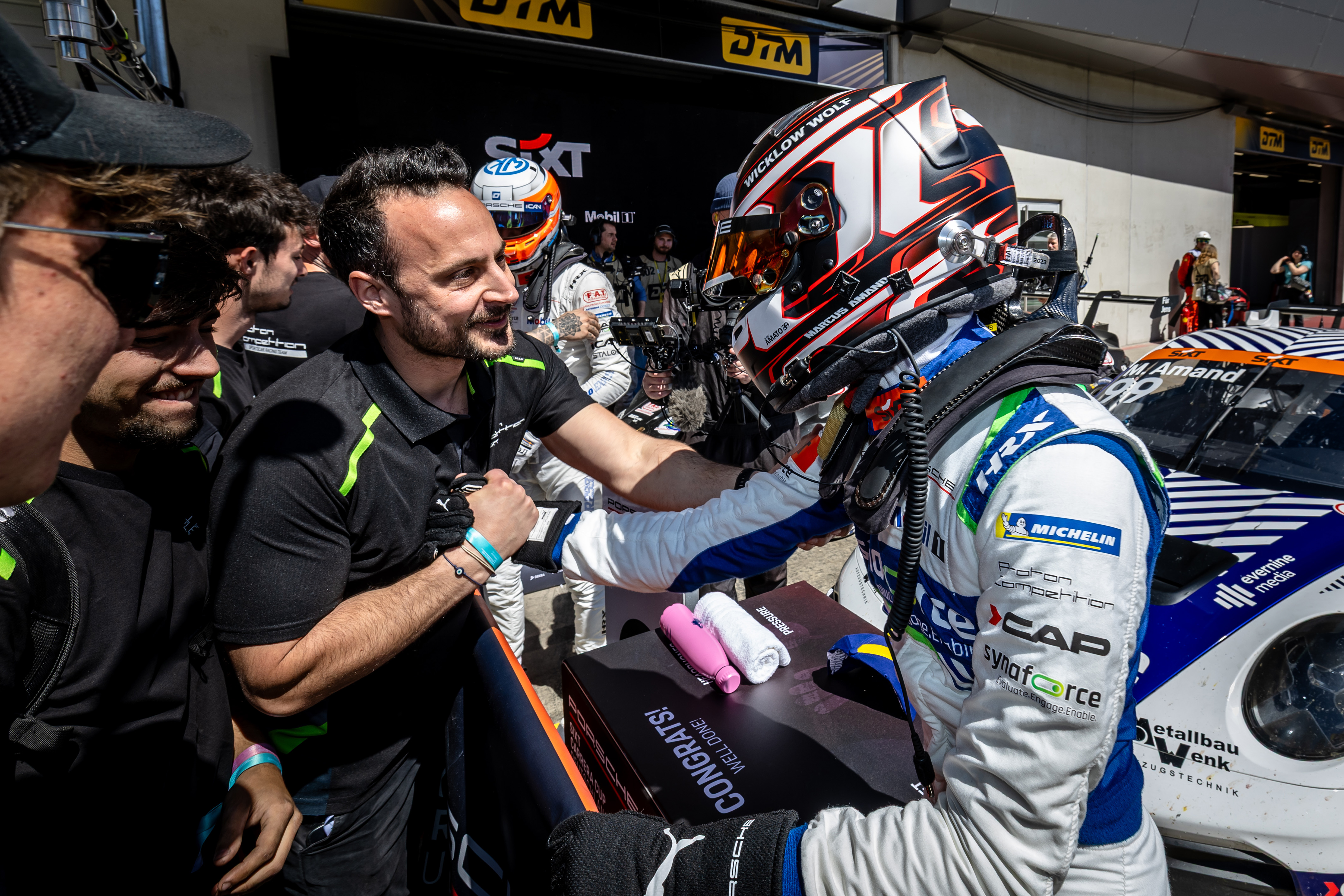 Team Proton greeting racing driver Marcus Sander at the pit box with welcome sign in the background, Synaforce Porsche with Evernine Media logo on the right